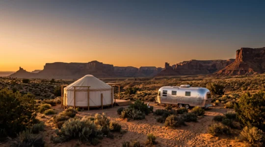 Wide editorial shot of a glamping yurt and a vintage Airstream trailer nestled in a dramatic American desert landscape at golden hour
